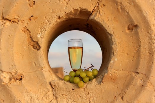 a glass of white wine and a bunch of grapes inside the a millstone for the pomace of grape juice