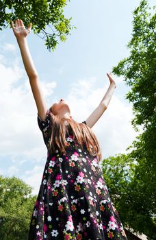 Teen girl with raised hands against blue cloudy sky