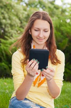 Teen girl reading electronic book outdoors