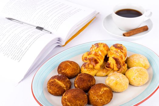 Cup of coffee with sweet cakes and book on table.