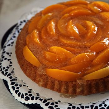 Colourful peach flan or tart with peach slices arranged in a whorled pattern served on a decorative doily on a buffet display or at a bakery