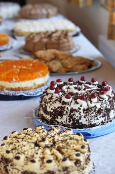 Buffet table with an assortment of delicious gourmet cakes at a wedding reception with focus to a creamy blackforest gateau decorated with cherries