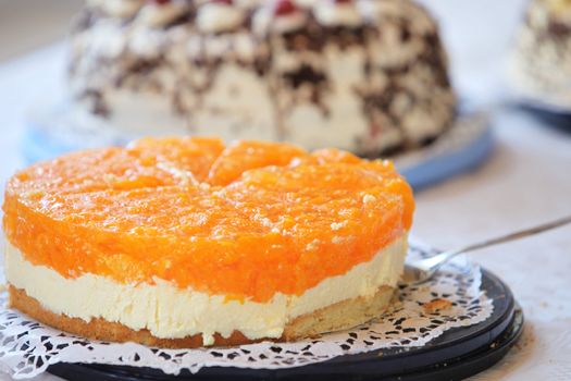 Tangy colourful citrus cheesecake with a vivid orange topping over a creamy cheese filling displayed on a buffet table of assorted cakes for dessert