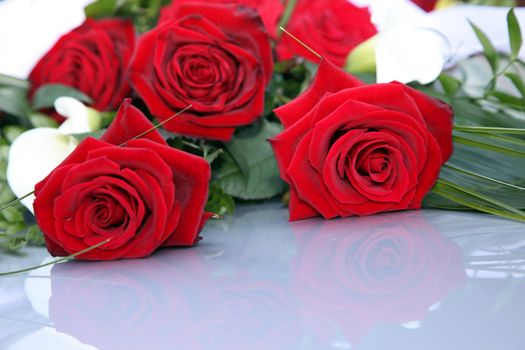 Romantic bouquet of fresh red roses at a wedding or as an anniversary gift lying on a reflective white table top with copyspace