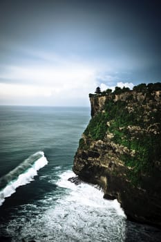 Steep coastal cliffs with green vegetation towering above the ocean with rolling waves and white breakers