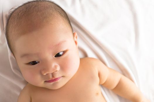 A cute asian baby resting on the bed looking down