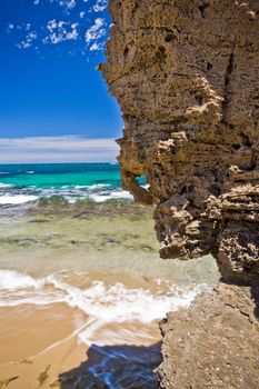 Interesting rough weathered rocky overhang on a tropical beach with clear surf lapping the golden sand and an azure ocean backdrop