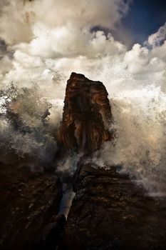 Dramatic image of waves breaking on a rock in a cloud pf spray under a stormy sky during a cyclone