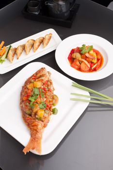 Freshly prepared Thai style whole fish red snapper dinner with sweet and sour shrimp and pan fried gyoza dumplings appetizer.  