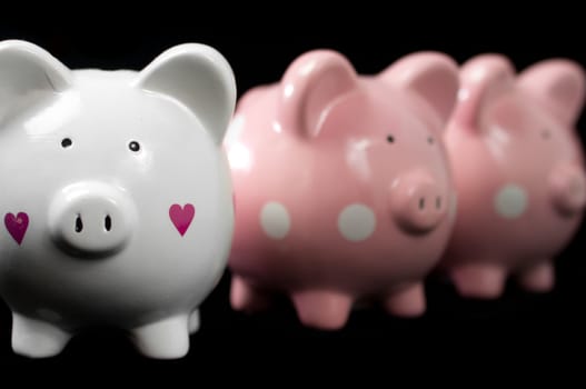 Three little piggy banks lined up. Unique white heart piggy in focus against black background