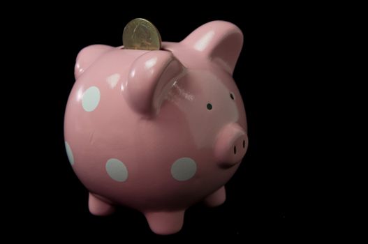 Pink Polka Dot  PIggy Bank with coin in slot on back background