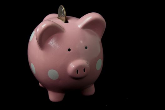 Pink Polka Dot  PIggy Bank with coin in slot on back background