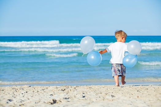 Back vie of cute little boy plays with ballons on the beach