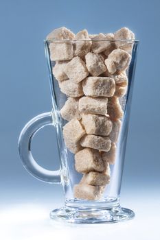 Cappuccino type of glass filled with brown sugar cubes on blue background.