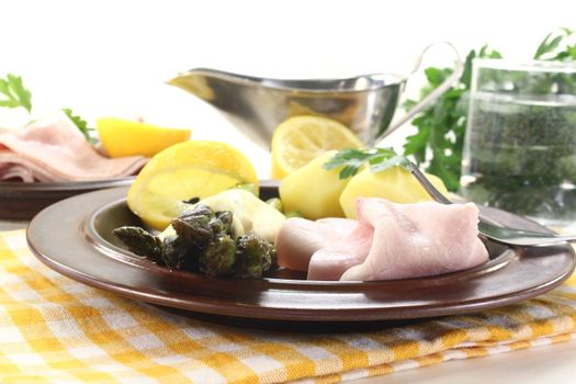 Asparagus with hollandaise sauce, potatoes and cooked ham on a light background