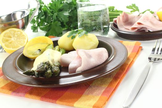 green Asparagus with hollandaise sauce, potatoes and delicious cooked ham on a bright background