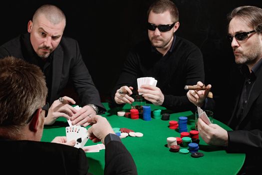 Photo of four men playing poker, smoking cigars and drinking whiskey. Focus is on the winning hand.