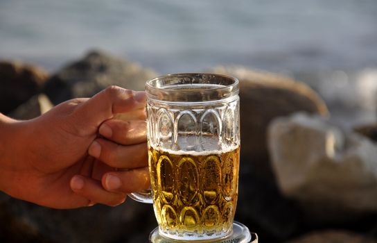 A mug of beer against rocks and the ocean