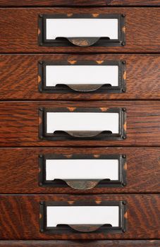 Vertical stack of five old oak flat file drawers with white empty tags in tarnished brass label holders.