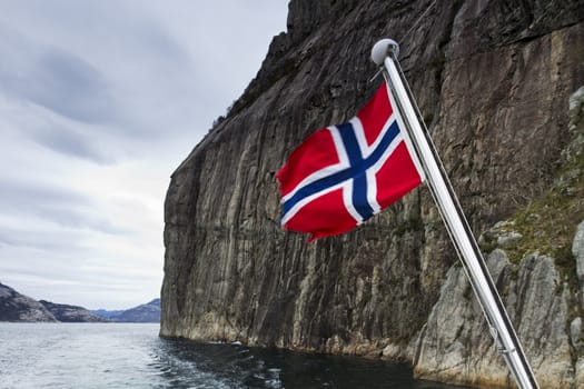 steep mountain over fjord with flag in foreground