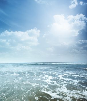 Vertical photo of the blue sea with foam and cloudy sky. Vibrant colors