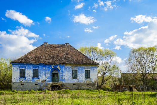 abandoned blue house against blue sky on green meadow