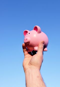 holding up a piggy bank against a pure blue sky background