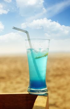Close-up photo of the glass with fresh cold cocktail at the summer beach. Vibrant colors