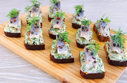 Snack rye bread with butter cream with herbs and herring spetsiyamina with a wooden board