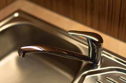 close-up of a chrome water faucet in a wooden kitchen