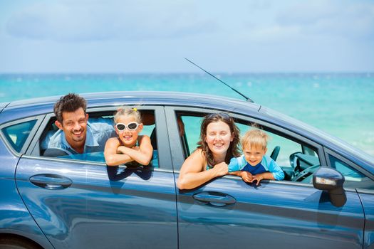 A family of four, mother, father, son and daughter driving in a car on a sunny day in hot location, backround sea