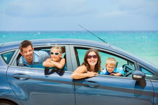 A family of four, mother, father, son and daughter driving in a car on a sunny day in hot location, backround sea