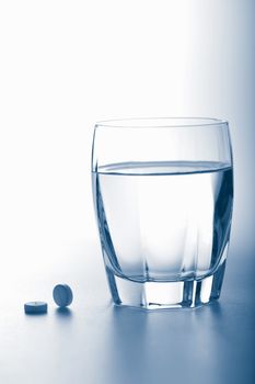 aspirin pills and glass of water toned blue