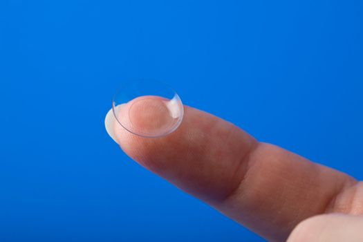 finger holding contact lens over blue background