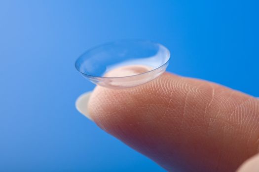 finger holding contact lens over blue background
