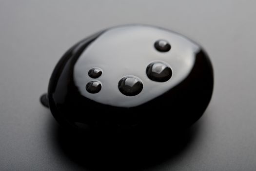 black shiny zen stone with water drops over black background