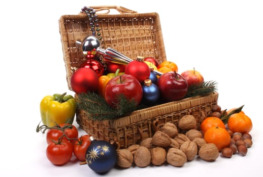 A picnic basket partially filled with Christmas balls and fruit over white. 