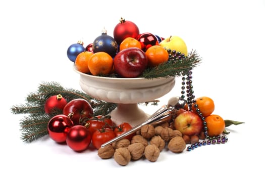 A fruit-dish partially filled with Christmas balls and fruit over white. 