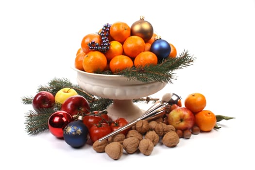 A fruit-dish partially filled with Christmas balls and fruit over white. 