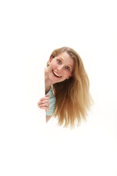 Attractive vivacious woman with a surprised expression peering round the side of a large blank white board