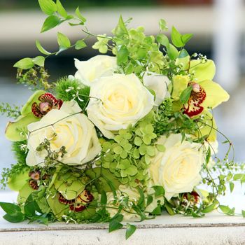 Closeup of a beautiful bouquet of cream coloured roses and green orchids with delicate foliage lying on a white surface