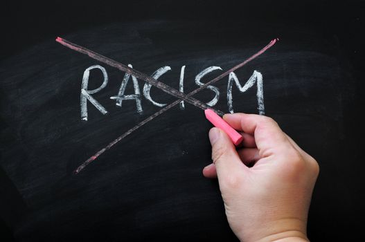 Cross out racism on a smudged blackboard background with red chalk holding in hand