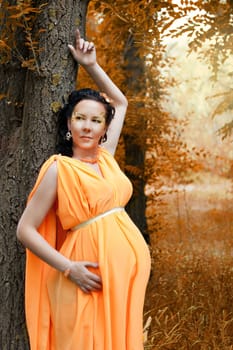 a pregnant woman standing next to a tree.