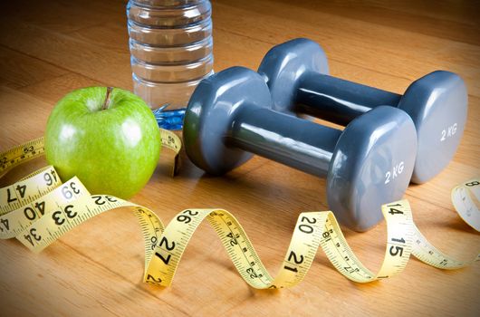 Pair of dumbbells, green apple, measuring tape and bottle of water. Exercise and healthy diet concept.