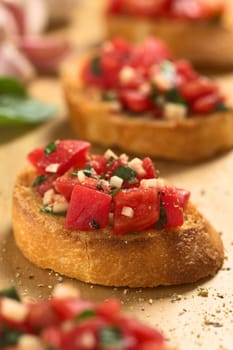 Fresh homemade crispy Italian antipasto called Bruschetta topped with tomato, garlic and basil on wooden board (Selective Focus, Focus on the front of the bruschetta one third into the image) 