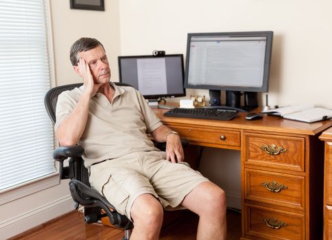 Senior caucasian man working from home in shorts with desk with two monitors
