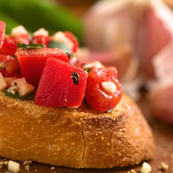 Fresh homemade crispy Italian antipasto called Bruschetta topped with tomato, garlic and basil on wooden board (Selective Focus, Focus on the tomato piece in the front) 