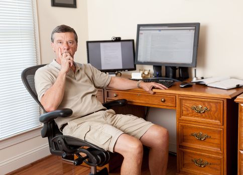 Senior caucasian man working from home in shorts with desk with two monitors