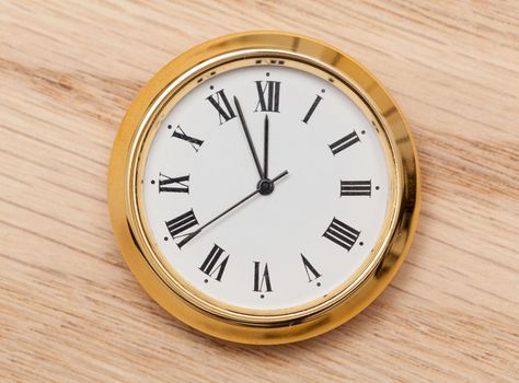 Small gold colored clock almost at midnight and laying on a wooden table