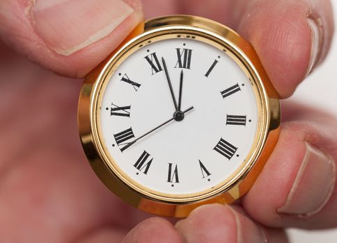 Small gold colored clock almost at midnight held by tips of fingers